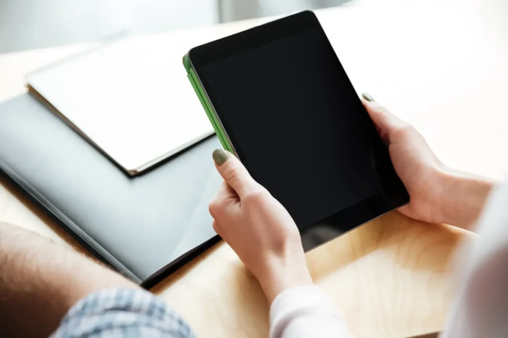 Eine Person hält ein schwarzes Tablet mit grünem Cover in den Händen.