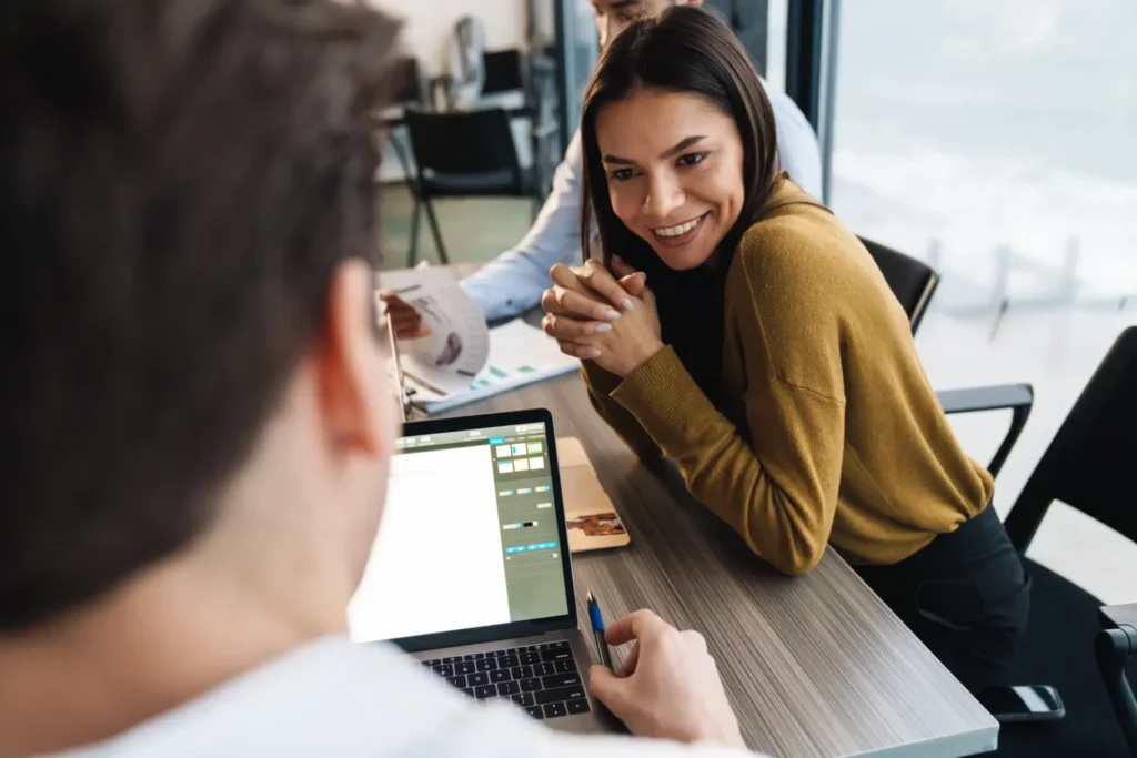Junge weibliche und männliche Kollegen sitzen an einem Tisch und arbeiten an einem Laptop.